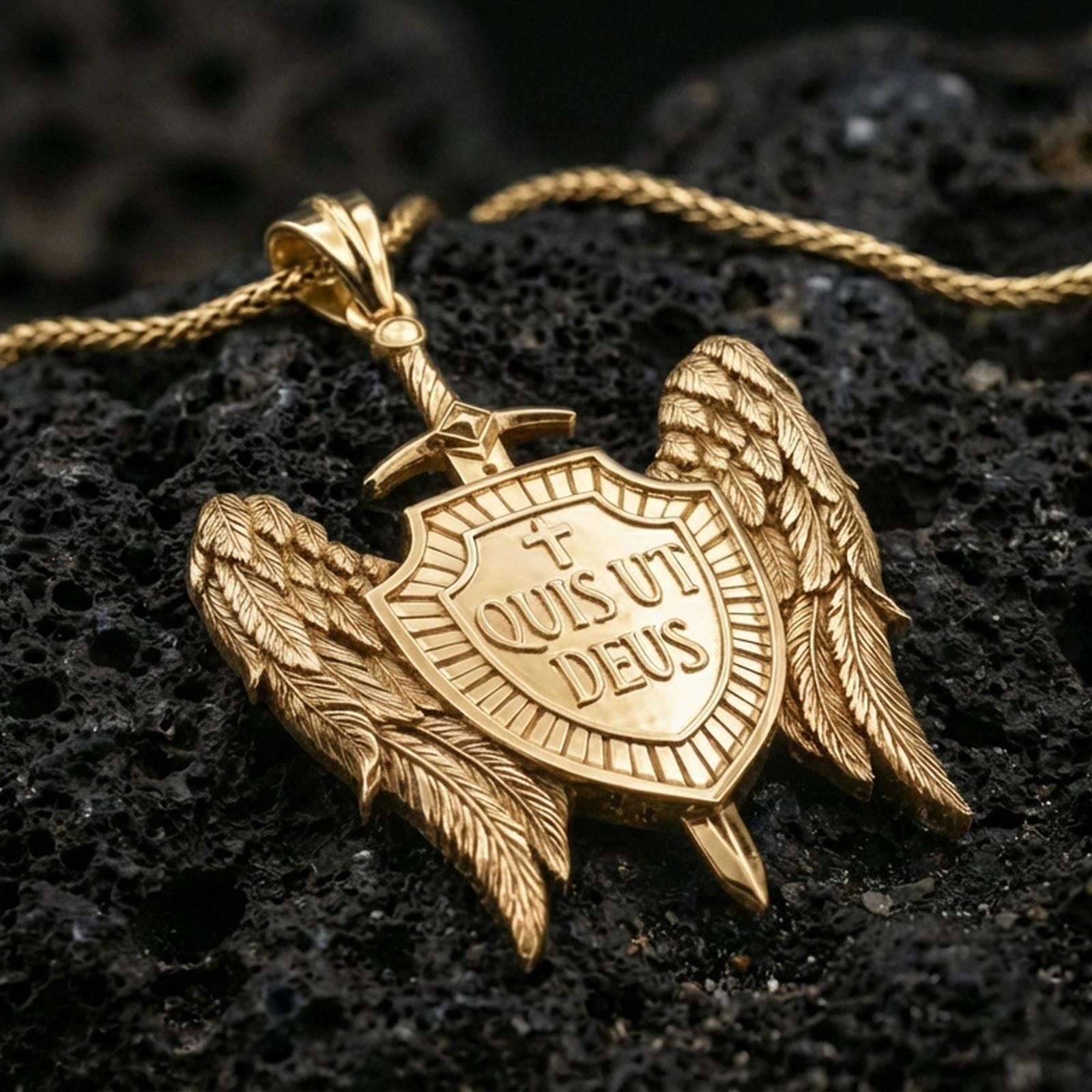Gold plated Saint Michael medal pendant with detailed feathered wings, sword, and engraved shield resting on black volcanic rock in a dramatic macro product image