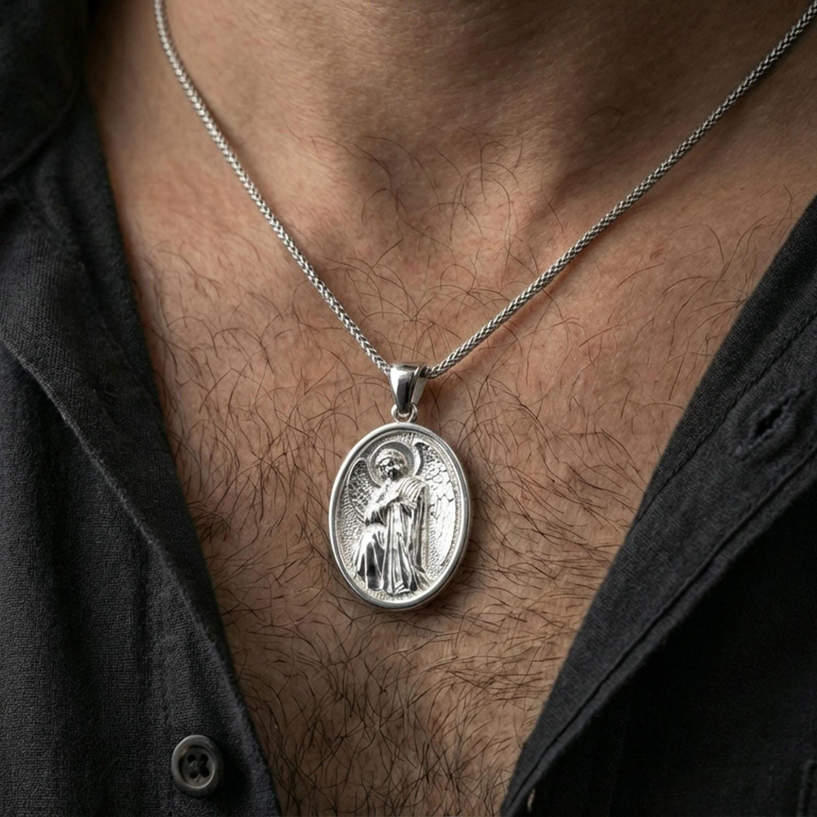 Polished silver oval angel pendant worn on the neck in a close lifestyle frame, highlighting the detailed winged figure and classic religious design