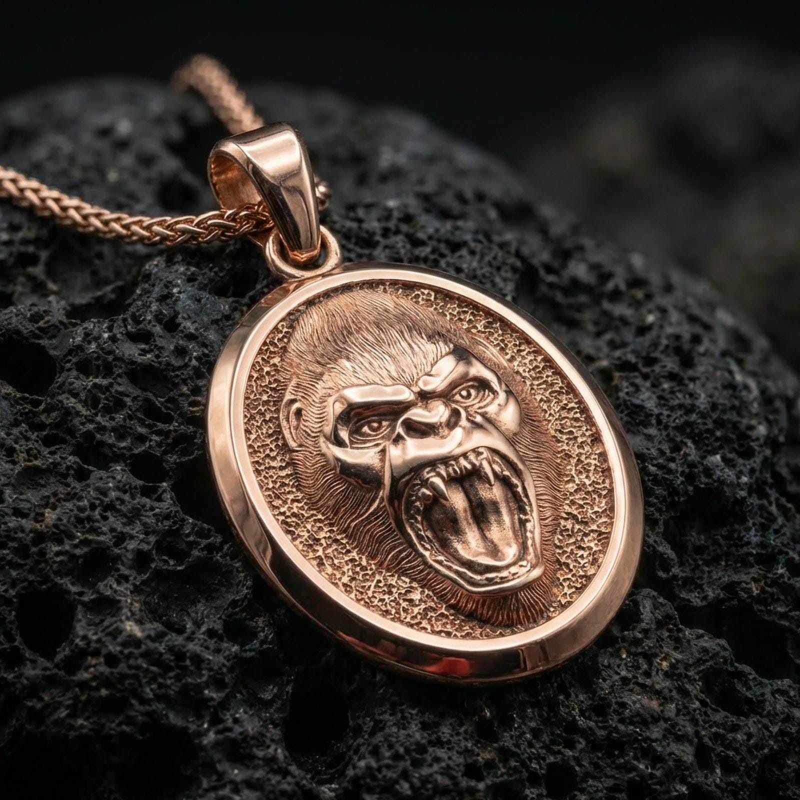 Rose gold plated roaring gorilla necklace with fierce open-mouth primate relief, detailed facial texture, and elegant oval medallion form resting on volcanic rock in an elegant close-up product presentation