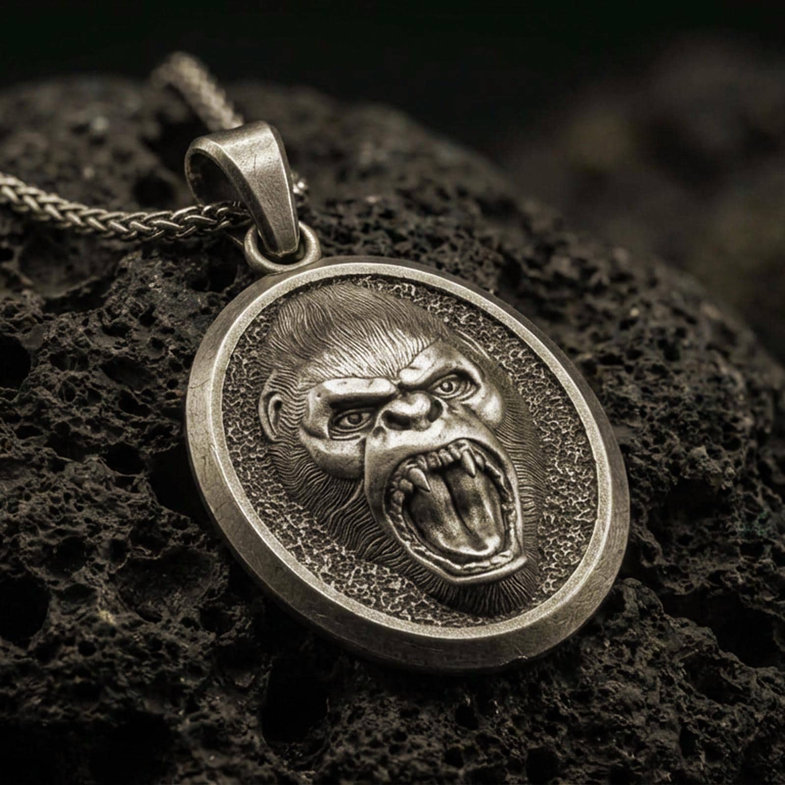 Bronze roaring gorilla pendant with fierce open-mouth ape relief, oval medallion frame, and bold primal animal silhouette displayed on dark volcanic rock in a close-up luxury jewelry composition