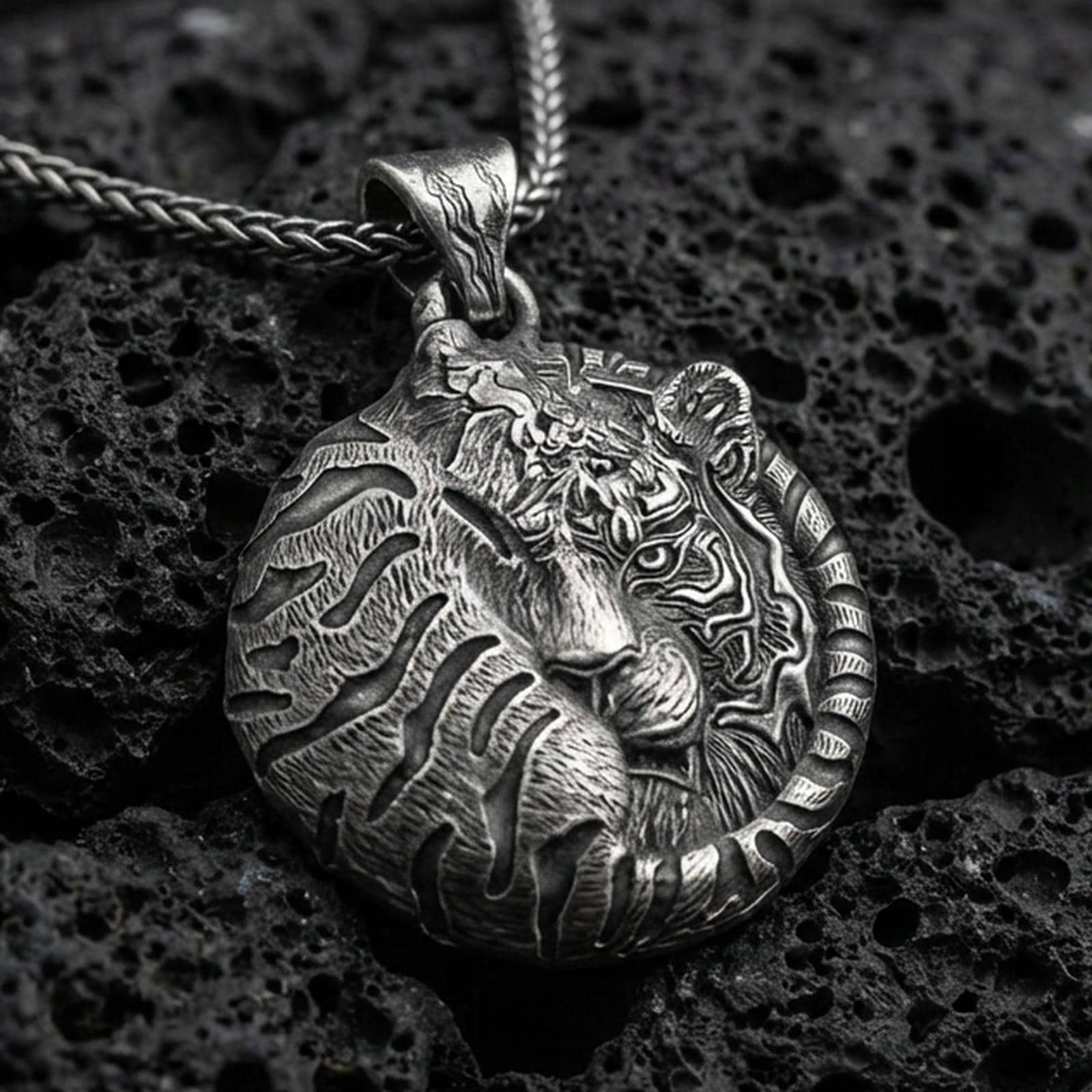 Oxidized tiger pendant with curled sleeping feline form, detailed stripe engraving, and round symbolic jungle silhouette displayed on dark volcanic rock in a close-up luxury jewelry composition