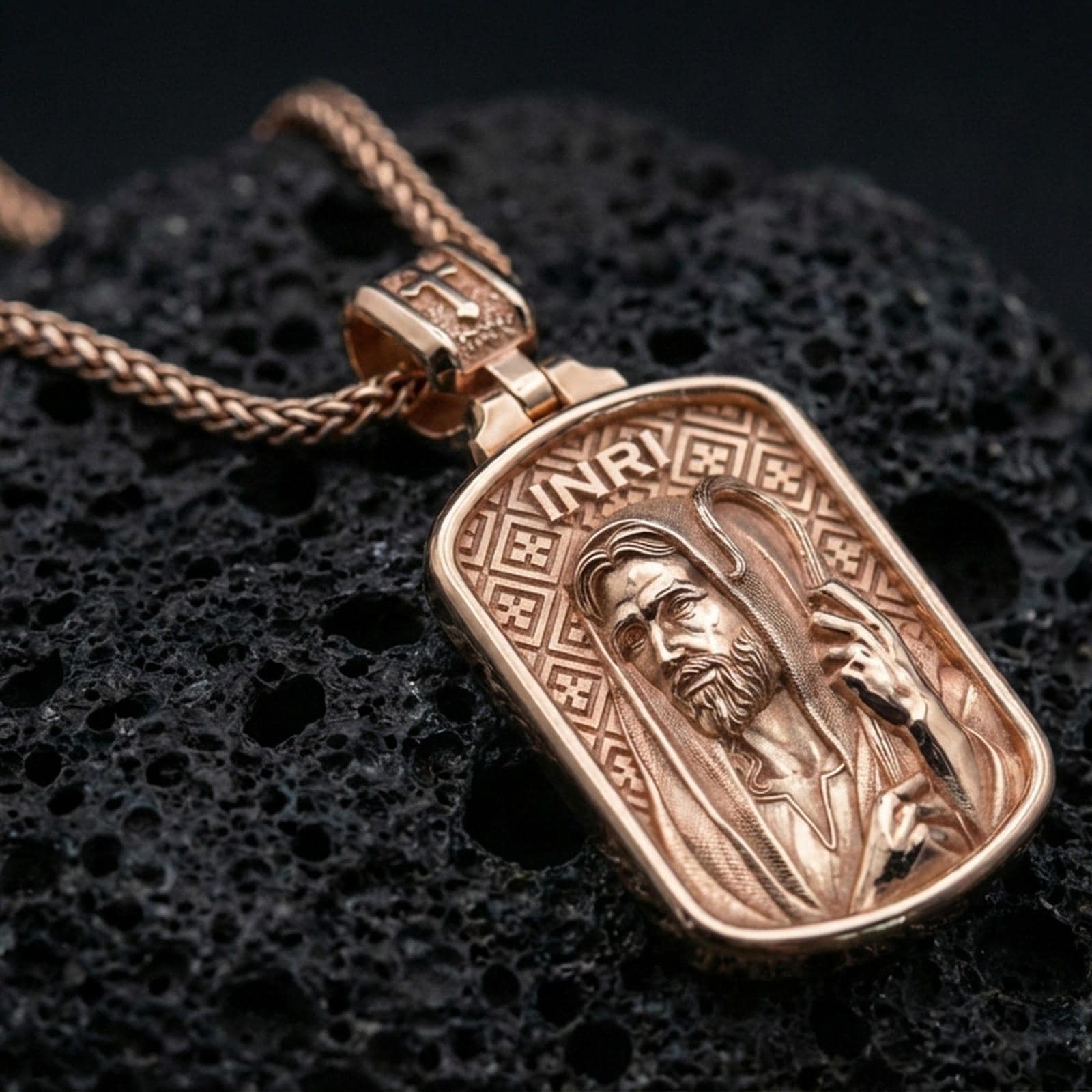 Rose gold plated devotional Jesus pendant with framed portrait, engraved background, and INRI inscription resting on volcanic rock in an elegant close-up product presentation