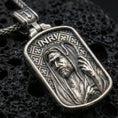 Load image into Gallery viewer, Oxidized Jesus pendant with INRI inscription and shepherd staff relief displayed on dark volcanic rock in a close-up luxury jewelry composition
