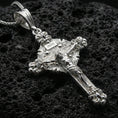 Load image into Gallery viewer, Polished silver crucifix pendant with sculpted Christ figure, floral gothic accents, and INRI detail placed on textured volcanic rock in a premium studio product shot
