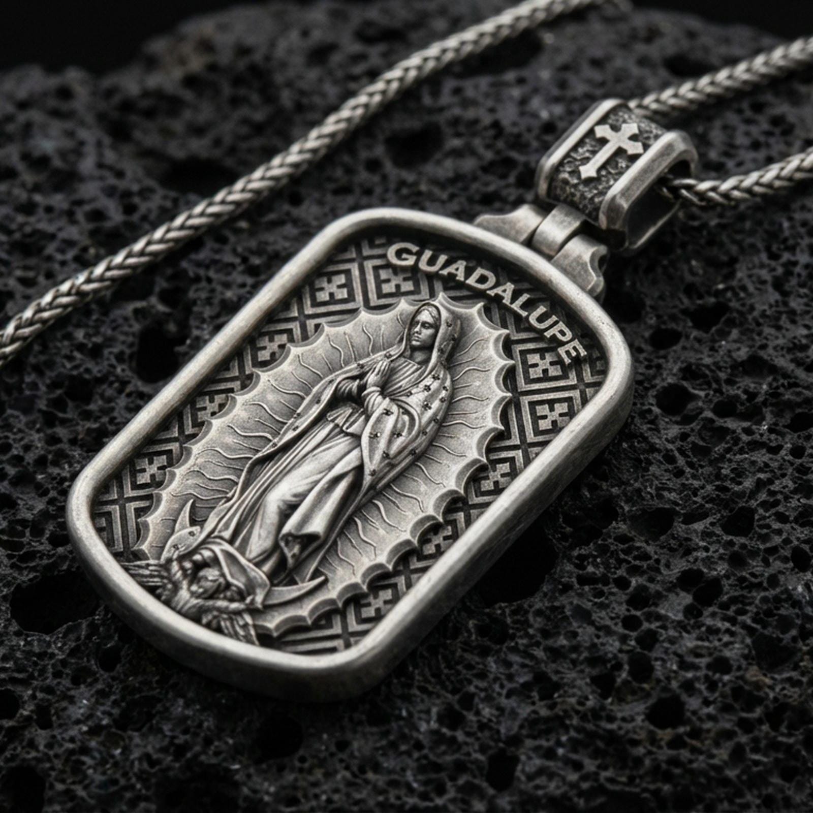 Oxidized Our Lady of Guadalupe pendant with framed devotional figure and Guadalupe inscription displayed on dark volcanic rock in a close-up luxury jewelry composition