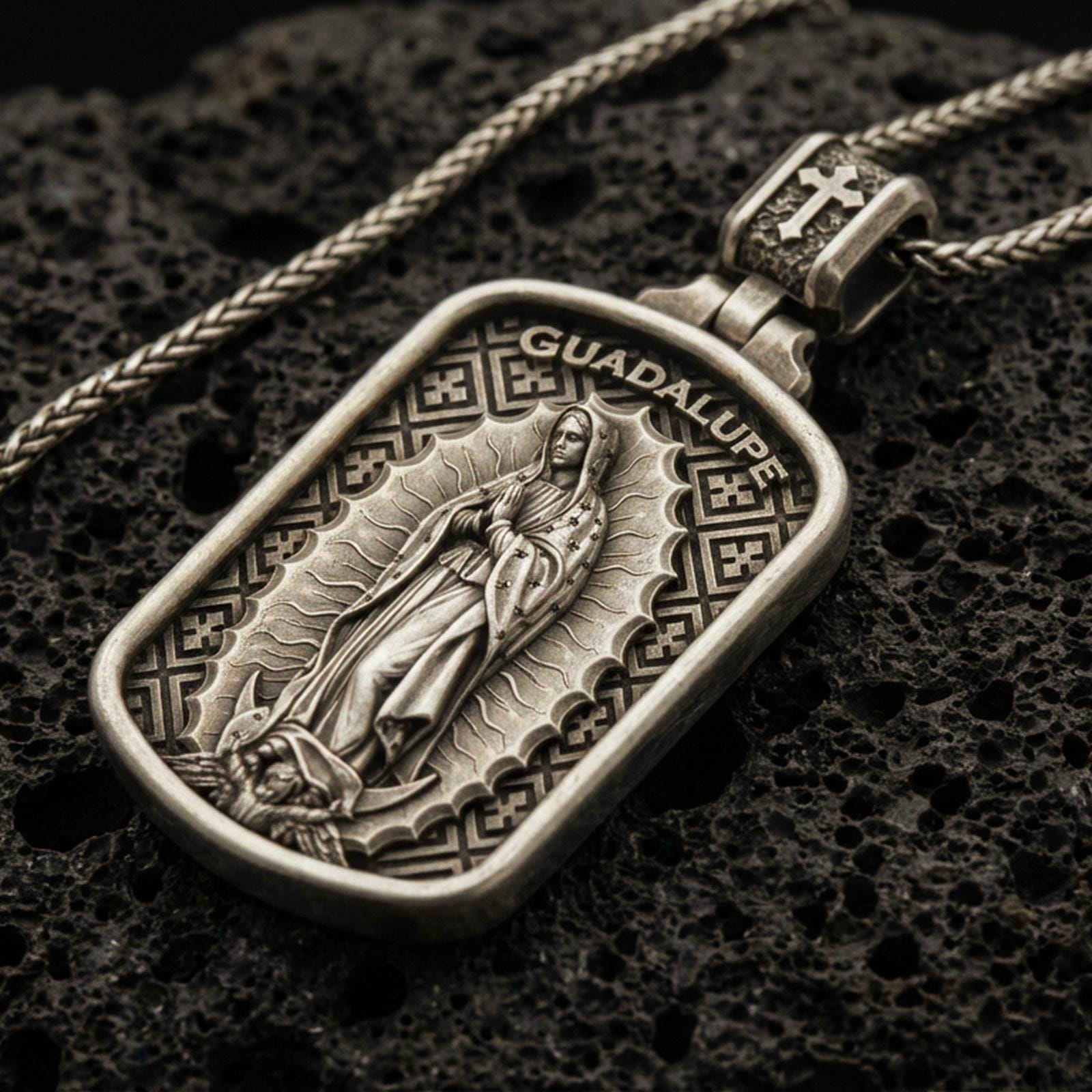 Bronze Our Lady of Guadalupe pendant with framed devotional figure and Guadalupe inscription displayed on dark volcanic rock in a close-up luxury jewelry composition