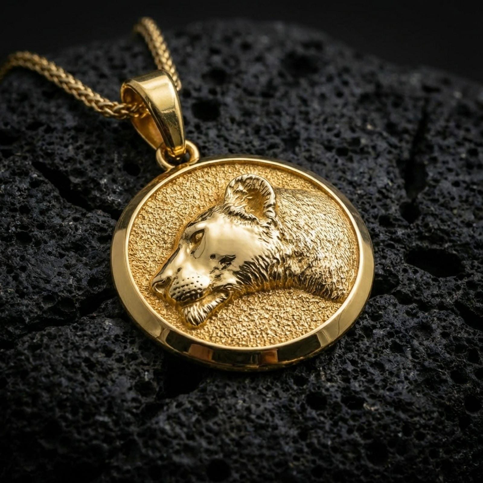 Gold plated lioness pendant with graceful feline profile, detailed fur relief, and elegant symbolic animal form showcased on black volcanic rock in a refined macro jewelry image