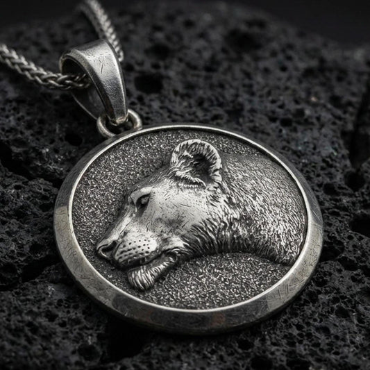 Oxidized lioness pendant with detailed feline profile, round medallion frame, and elegant wild cat silhouette displayed on dark volcanic rock in a close-up luxury jewelry composition