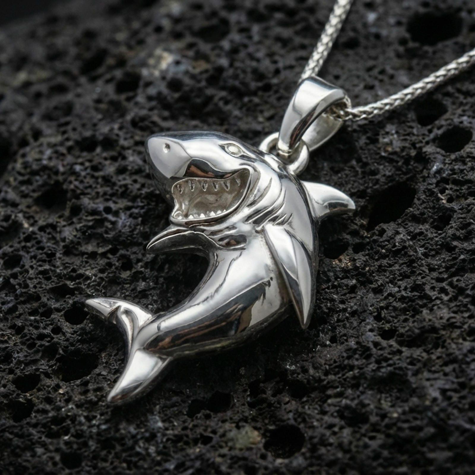 Polished silver shark necklace with detailed teeth, dynamic swimming pose, and bold ocean-inspired animal form placed on textured volcanic rock in a premium studio product shot