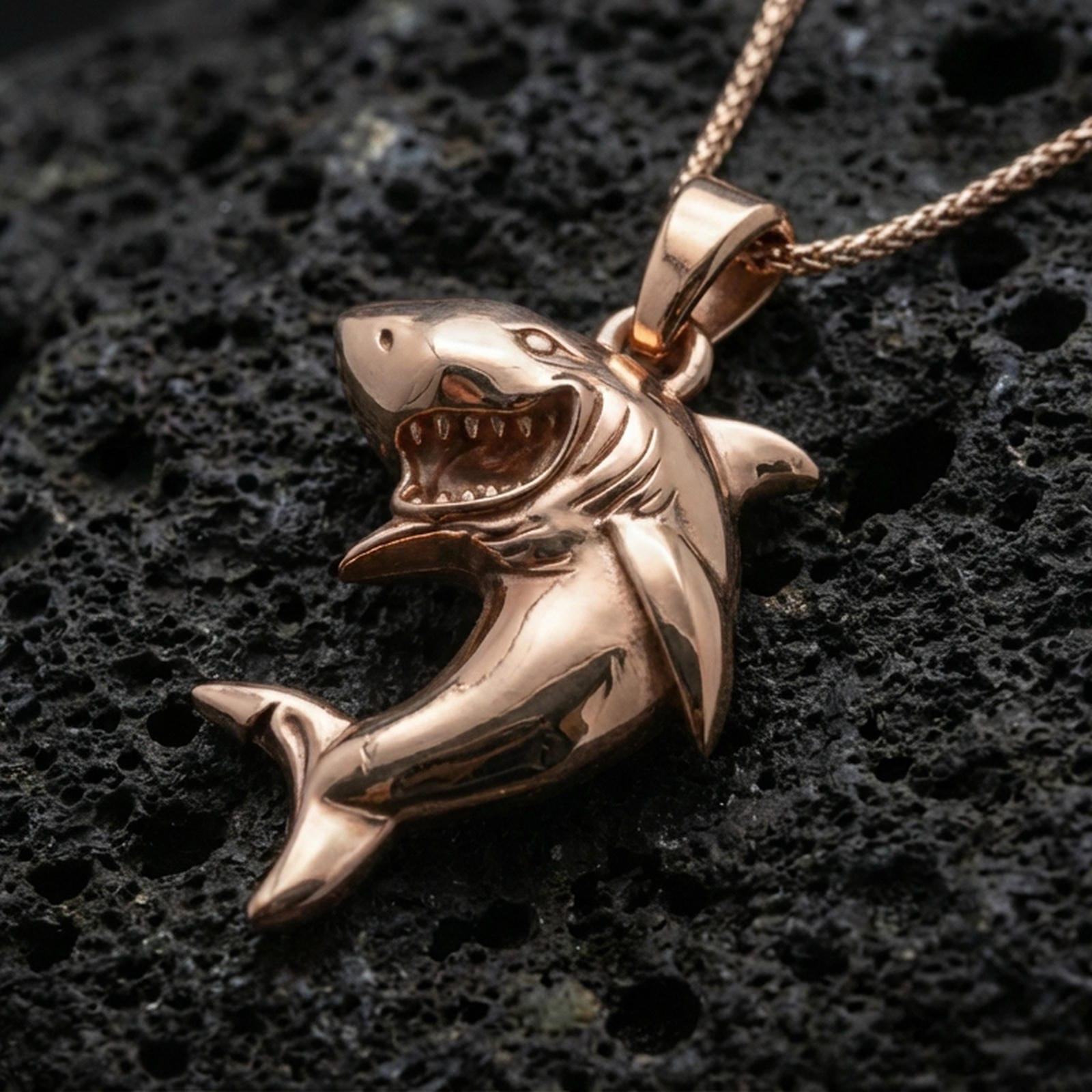 Rose gold plated shark necklace with playful shark form, detailed fin structure, and bold aquatic animal silhouette resting on volcanic rock in an elegant close-up product presentation