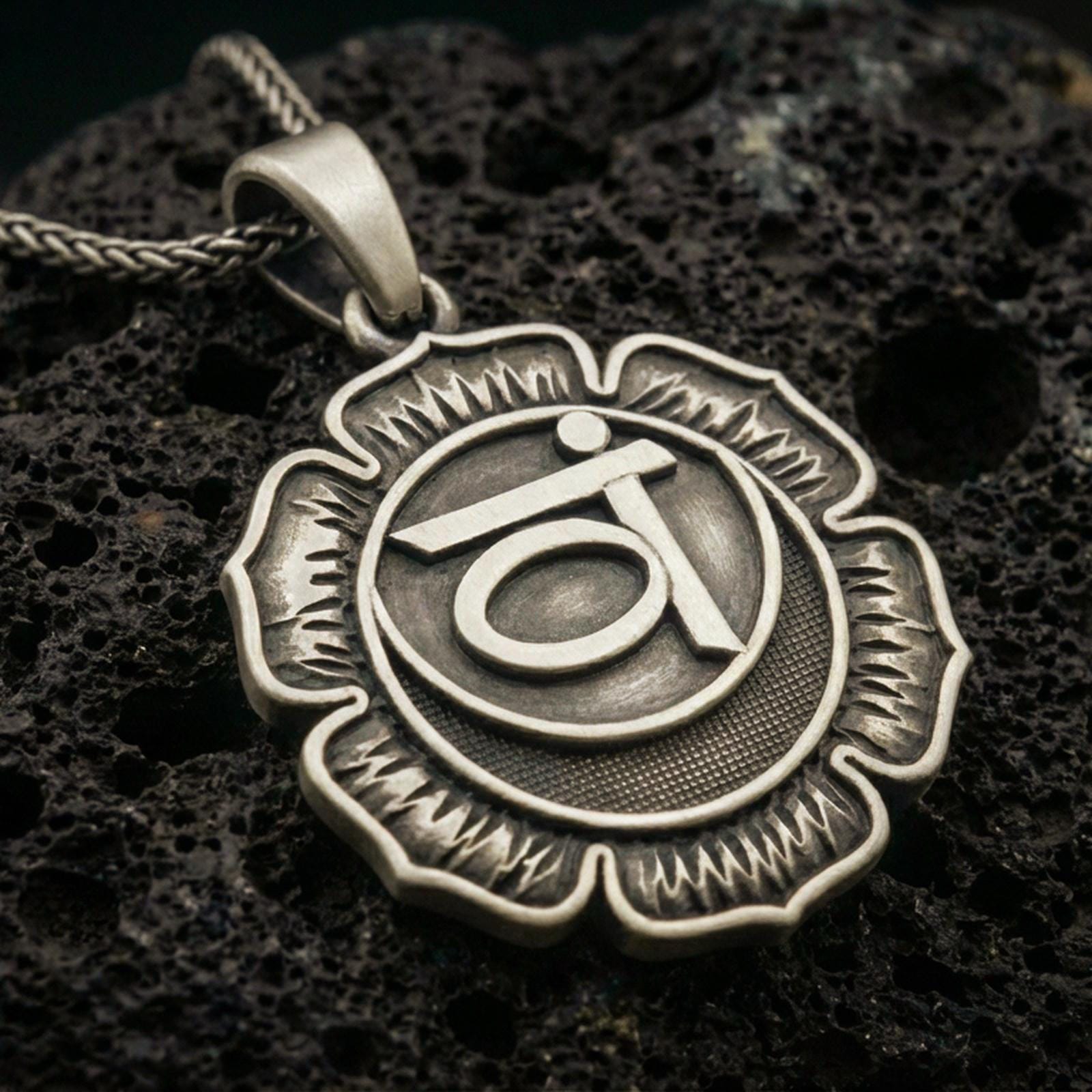 Bronze throat chakra pendant with lotus flower silhouette and sacred symbol relief displayed on dark volcanic rock in a close-up luxury jewelry composition