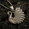 Load image into Gallery viewer, Bronze swan pendant with detailed feather engraving, graceful curved neck, and elegant bird silhouette displayed on dark volcanic rock in a close-up luxury jewelry composition
