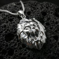 Load image into Gallery viewer, Polished silver geometric lion necklace with faceted low poly lion face, sharp angular contours, and modern predator head design placed on textured volcanic rock in a premium studio product shot

