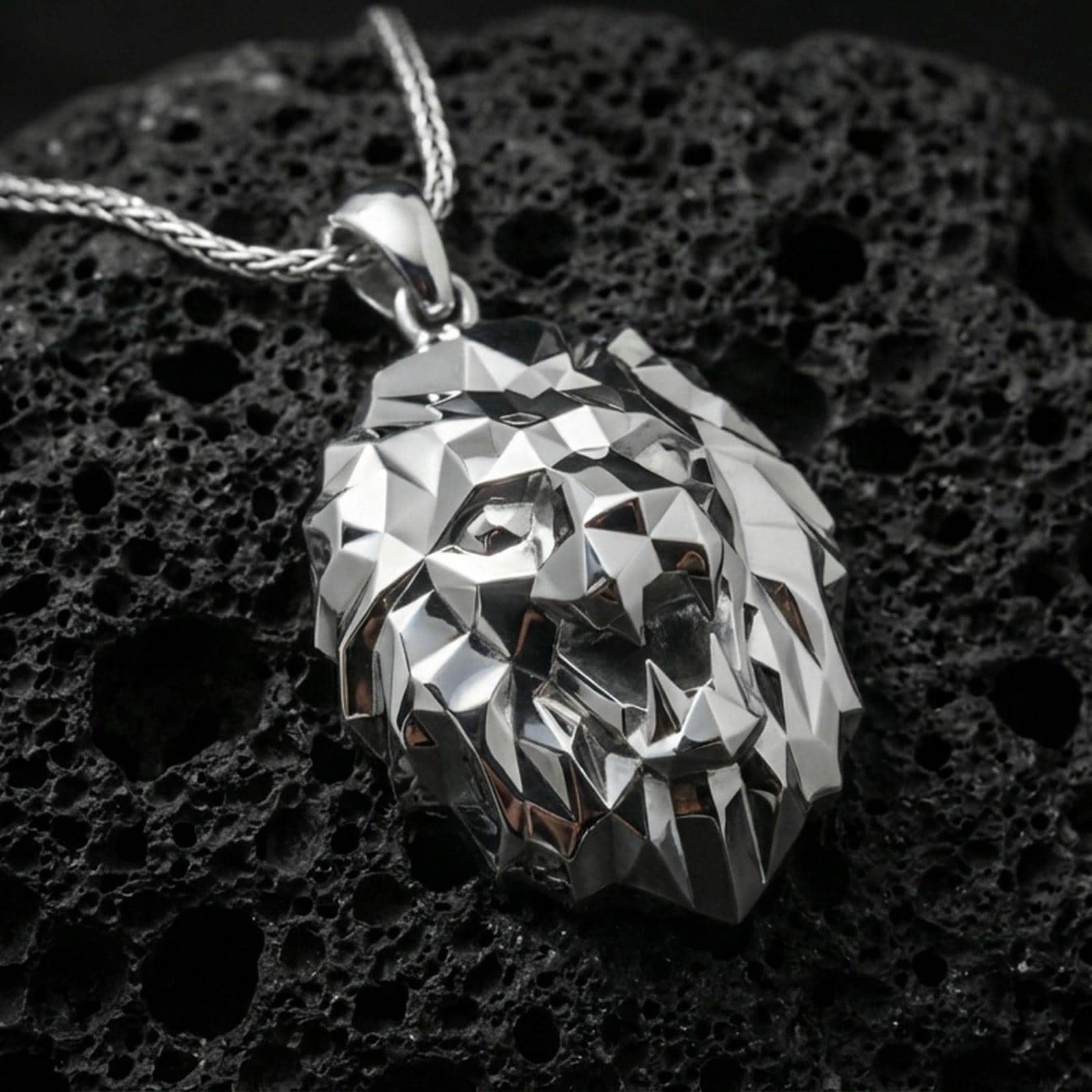 Polished silver geometric lion necklace with faceted low poly lion face, sharp angular contours, and modern predator head design placed on textured volcanic rock in a premium studio product shot