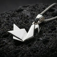 Load image into Gallery viewer, Polished silver origami swan necklace with sharp folded contours, abstract geometric bird form, and minimalist sculptural design placed on textured volcanic rock in a premium studio product shot
