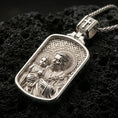 Load image into Gallery viewer, Polished silver Saint Joseph medallion with Child Jesus, radiant halo relief, and rounded rectangular frame placed on textured volcanic rock in a premium studio product shot
