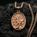 Load image into Gallery viewer, Rose gold plated oval religious pendant with sculpted saint relief, lion symbol, and open book detail resting on volcanic rock in an elegant close-up product presentation

