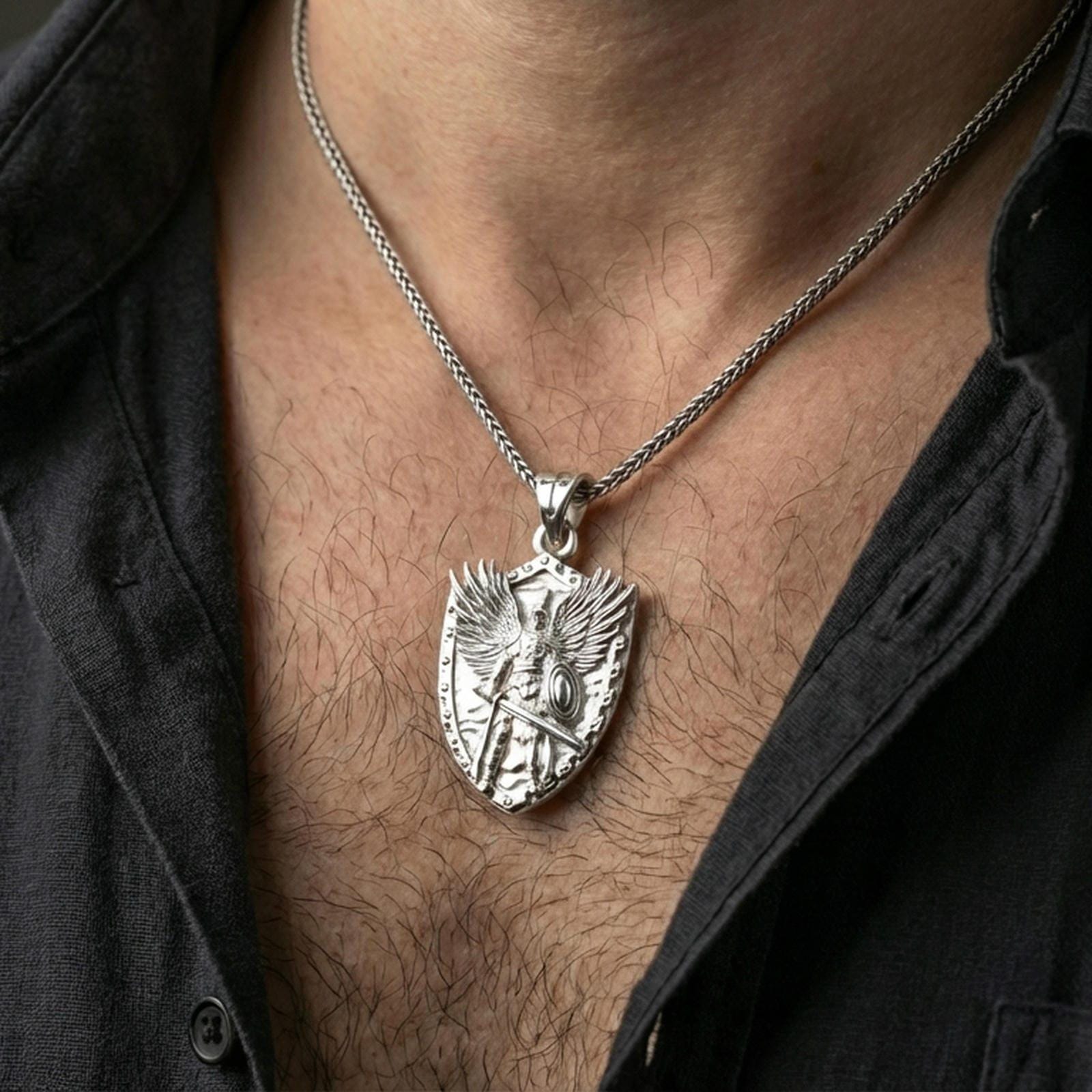 Polished silver Saint Michael pendant with winged warrior relief worn on the neck in a close lifestyle frame, highlighting the shield silhouette and guardian symbolism