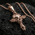 Load image into Gallery viewer, Rose gold plated gothic skull pendant with dramatic cross silhouette, sculpted skull relief, and intricate engraved texture resting on volcanic rock in an elegant close-up product presentation
