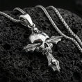 Load image into Gallery viewer, Polished silver gothic cross necklace with central skull motif, carved cross arms, and sculpted ornamental details placed on textured volcanic rock in a premium studio product shot
