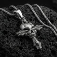 Load image into Gallery viewer, Oxidized gothic skull cross pendant with layered skull details and dark textured relief displayed on dark volcanic rock in a close-up luxury jewelry composition
