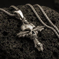Load image into Gallery viewer, Bronze gothic skull cross pendant with layered skull details and dark textured relief displayed on dark volcanic rock in a close-up luxury jewelry composition
