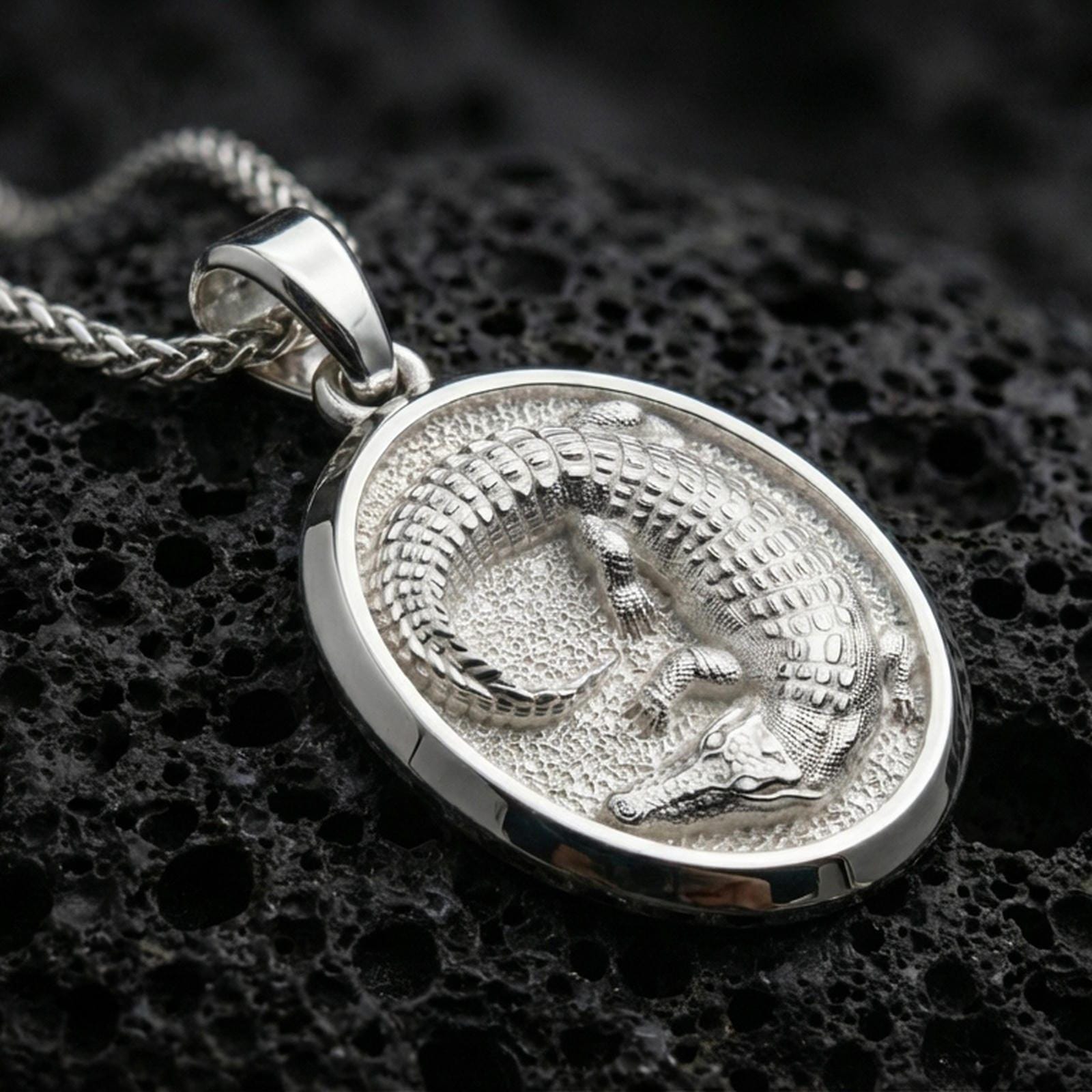 Sterling silver crocodile pendant necklace in polished silver on a dark volcanic rock surface, captured in a centered macro product shot.