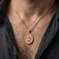 Load image into Gallery viewer, Rose gold plated Jesus resurrection pendant with haloed figure and banner detail worn on the neck in a refined lifestyle shot with a warm and elegant presentation
