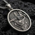 Load image into Gallery viewer, Oxidized resurrection medal pendant with risen Christ, cross staff, and halo detail displayed on dark volcanic rock in a close-up luxury jewelry composition
