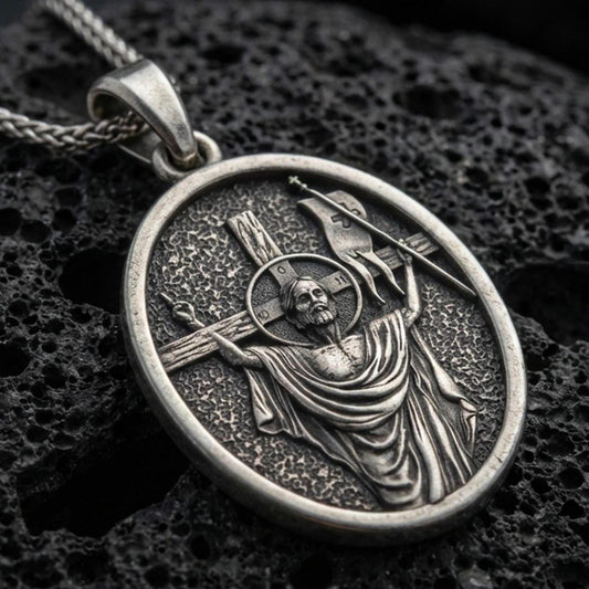 Oxidized resurrection medal pendant with risen Christ, cross staff, and halo detail displayed on dark volcanic rock in a close-up luxury jewelry composition