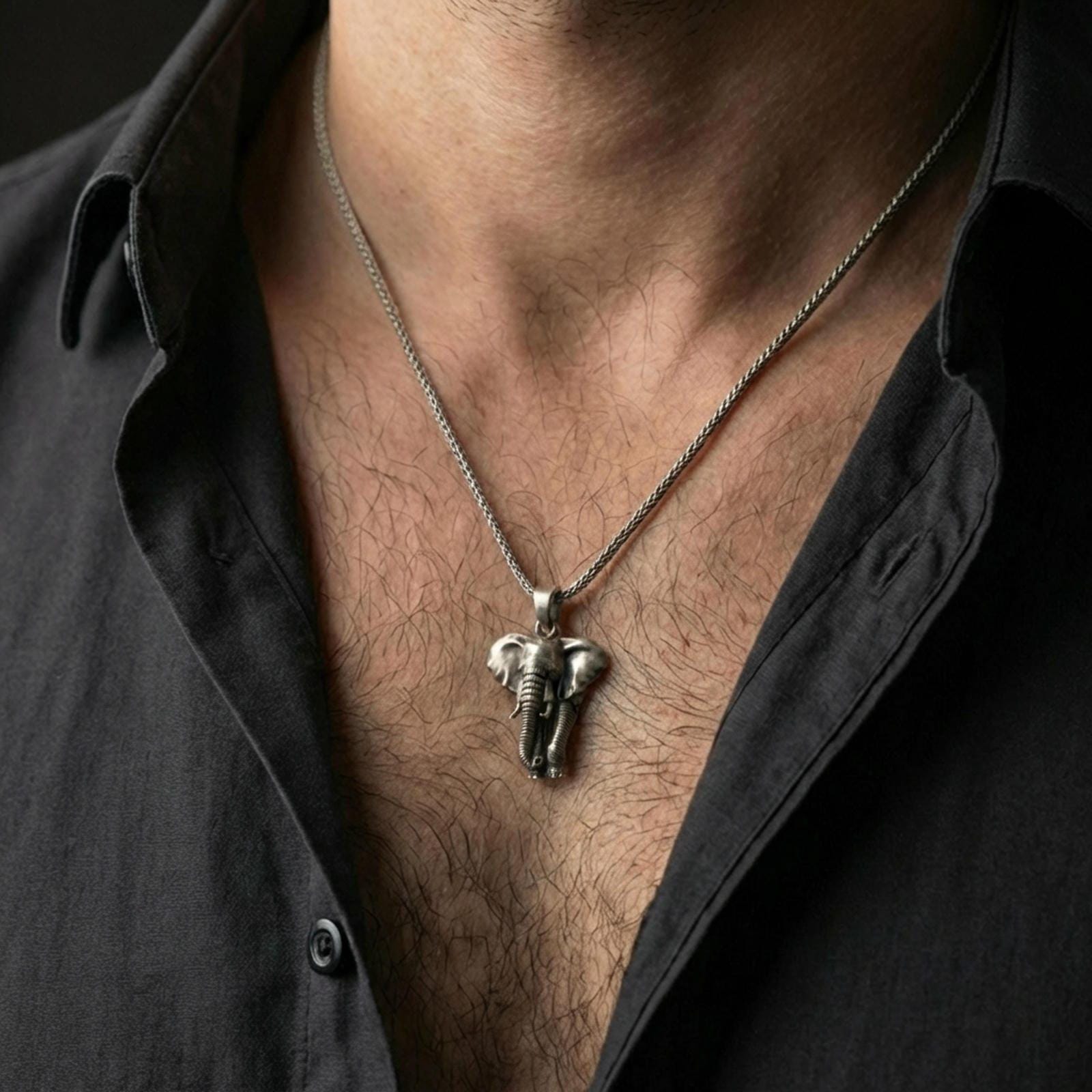 Oxidized elephant pendant necklace worn on the neck, styled in a dark lifestyle portrait with an open shirt and masculine presentation.