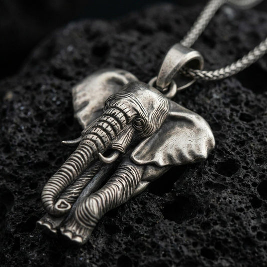 Sterling silver elephant pendant necklace with an oxidized finish resting on textured volcanic rock, captured in a close-up premium studio composition.