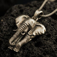 Load image into Gallery viewer, Bronze elephant pendant necklace with an oxidized finish resting on textured volcanic rock, captured in a close-up premium studio composition.
