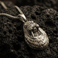 Load image into Gallery viewer, Bronze walrus pendant necklace with an oxidized finish resting on textured volcanic rock, captured in a close-up premium studio composition.
