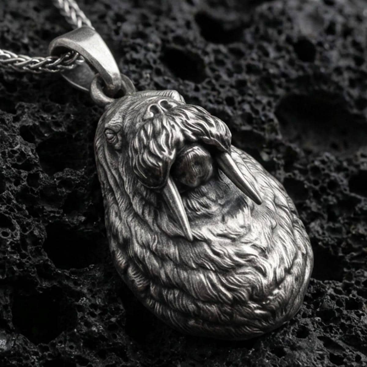 Sterling silver walrus pendant necklace with an oxidized finish resting on textured volcanic rock, captured in a close-up premium studio composition.