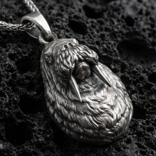 Sterling silver walrus pendant necklace with an oxidized finish resting on textured volcanic rock, captured in a close-up premium studio composition.