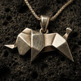 Load image into Gallery viewer, Bronze origami elephant pendant necklace with an oxidized finish resting on textured volcanic rock, captured in a close-up premium studio composition.
