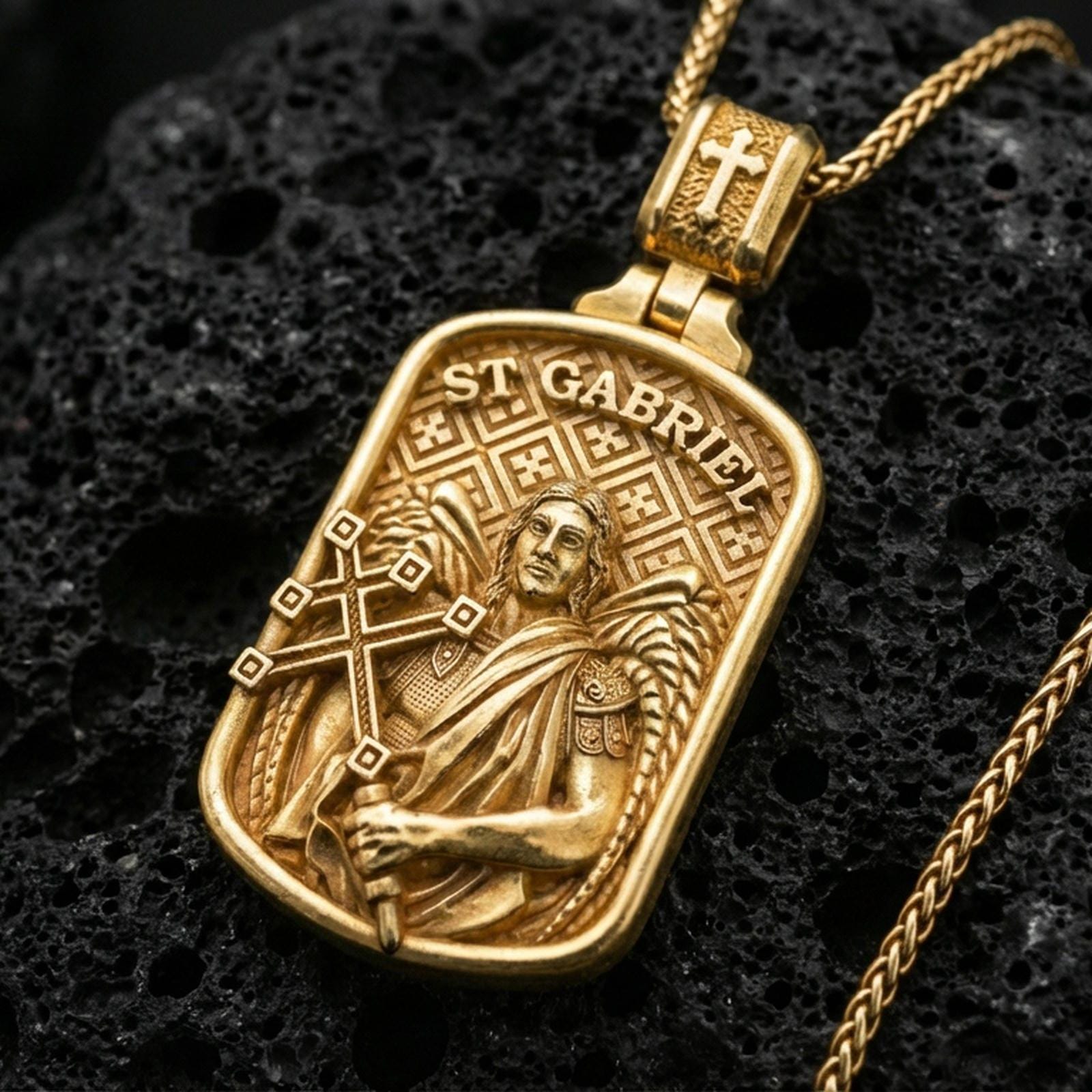 Gold plated Saint Gabriel necklace with angel relief, ornate cross staff, and engraved saint name showcased on black volcanic rock in a refined macro jewelry image
