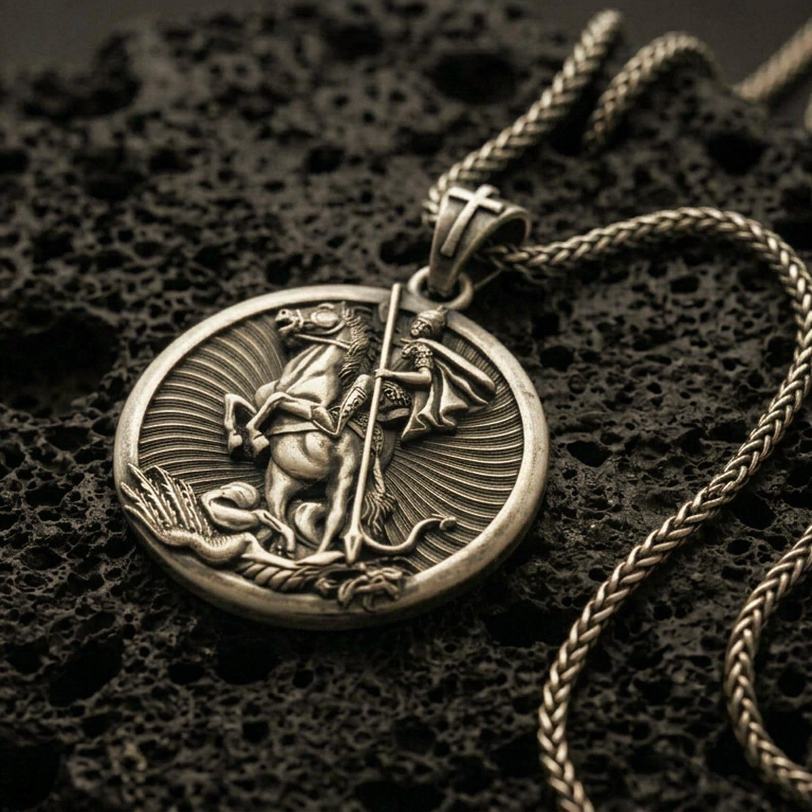 Bronze Saint George pendant with mounted warrior relief, spear detail, and round medallion design displayed on dark volcanic rock in a close-up luxury jewelry composition