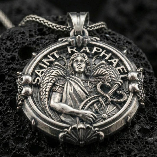 Oxidized Saint Raphael pendant with winged archangel figure, healing staff with serpent, and Saint Raphael inscription displayed on dark volcanic rock in a close-up luxury jewelry composition