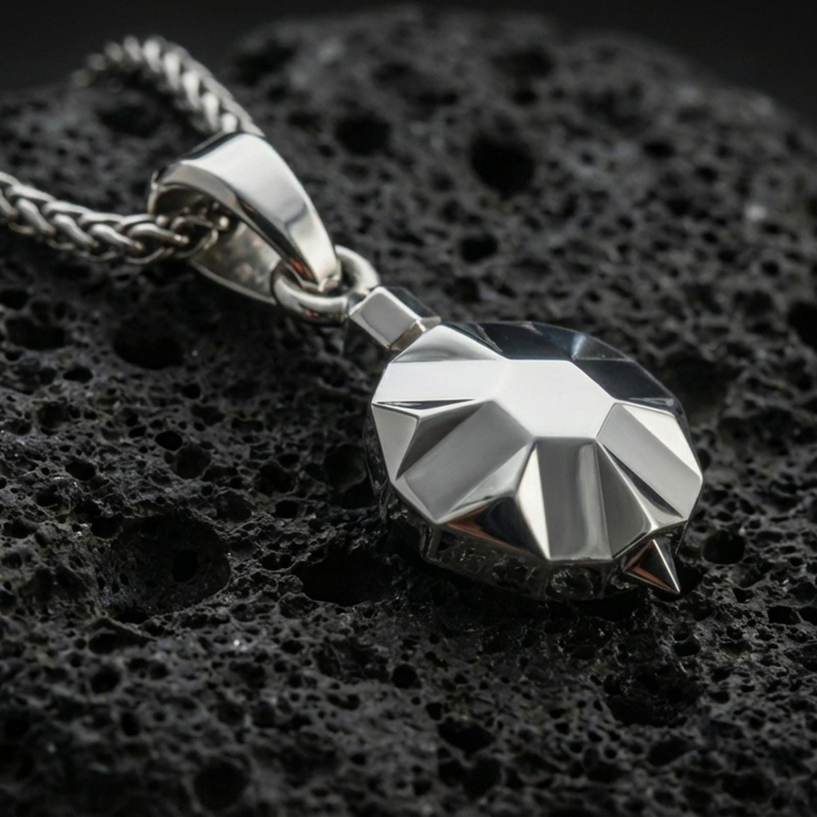 Polished silver origami tortoise pendant necklace displayed on black volcanic rock, shown in a refined macro product shot with crisp geometric facets.