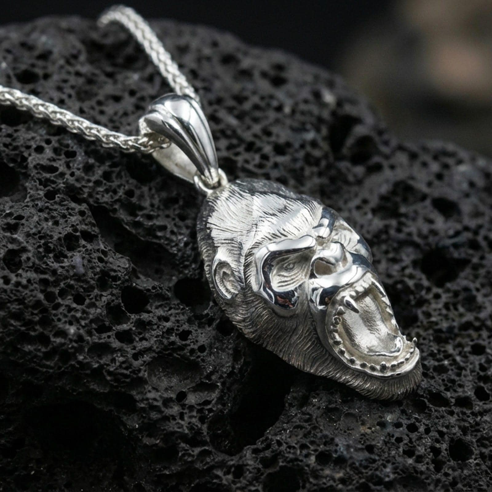 Polished silver gorilla head pendant necklace displayed on black volcanic rock, shown in a refined macro product shot with detailed facial sculpting.