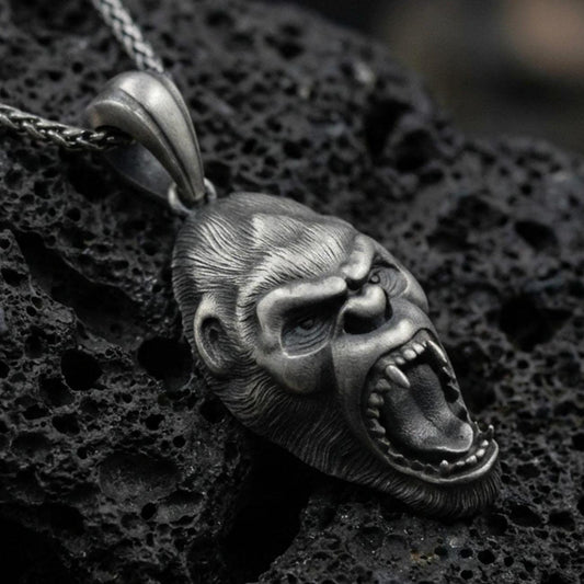 Sterling silver gorilla head pendant necklace with an oxidized finish resting on textured volcanic rock, captured in a close-up premium studio composition.