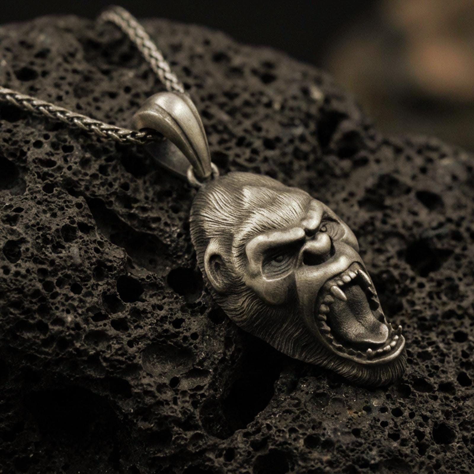 Bronze gorilla head pendant necklace with an oxidized finish resting on textured volcanic rock, captured in a close-up premium studio composition.