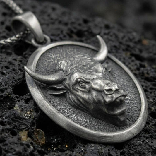 Sterling silver bull pendant necklace with an oxidized finish resting on textured volcanic rock, captured in a close-up premium studio composition.