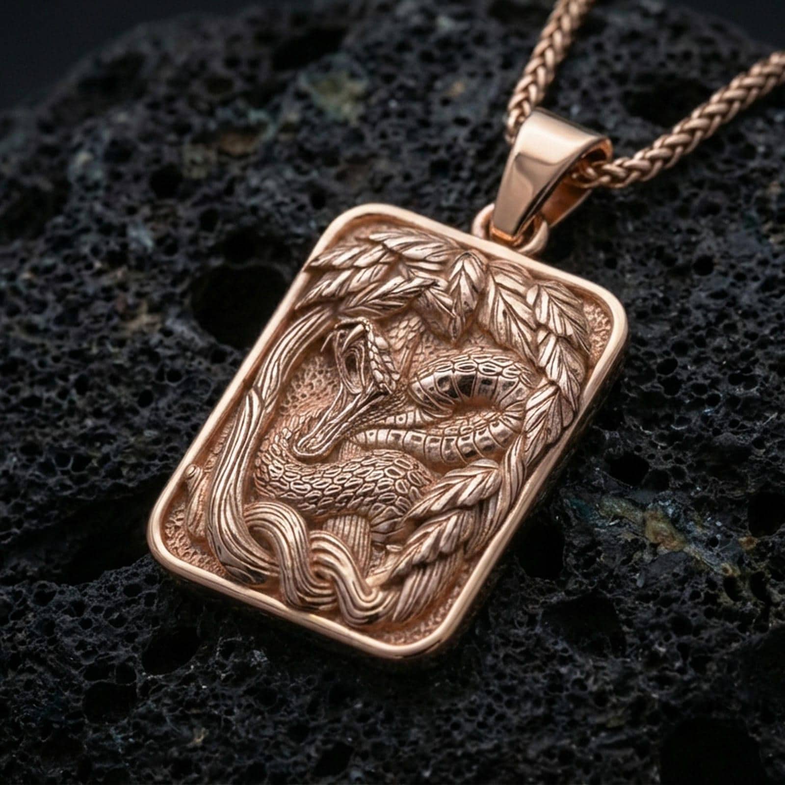 Rose gold plated cobra pendant necklace on dark volcanic rock, photographed in a detailed premium studio macro view.