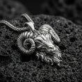 Load image into Gallery viewer, Sterling silver ram head pendant necklace with an oxidized finish resting on textured volcanic rock, captured in a close-up premium studio composition.
