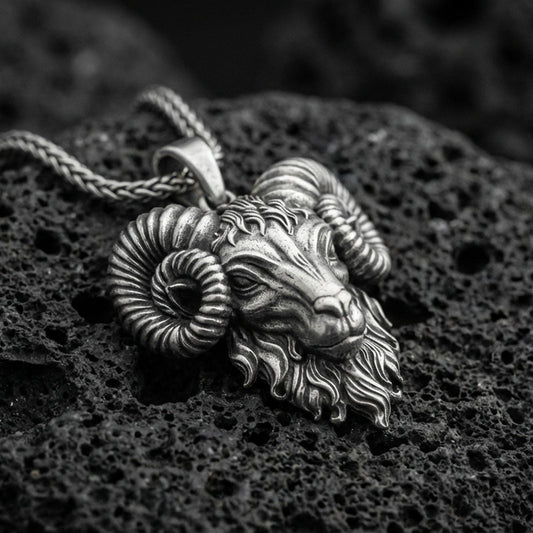 Sterling silver ram head pendant necklace with an oxidized finish resting on textured volcanic rock, captured in a close-up premium studio composition.