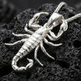 Load image into Gallery viewer, Polished silver scorpion pendant necklace displayed on black volcanic rock, shown in a refined macro product shot with detailed claws and segmented tail.
