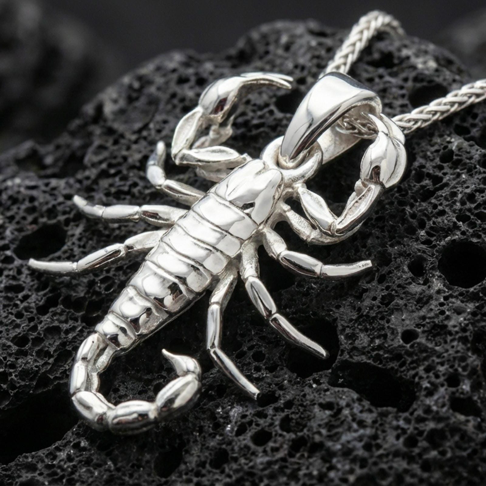 Polished silver scorpion pendant necklace displayed on black volcanic rock, shown in a refined macro product shot with detailed claws and segmented tail.